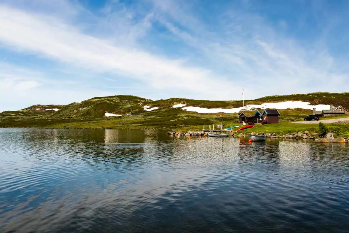 Små hytter ved innsjøen og båter på en solrik dag nær Norges fjellrute RV7.