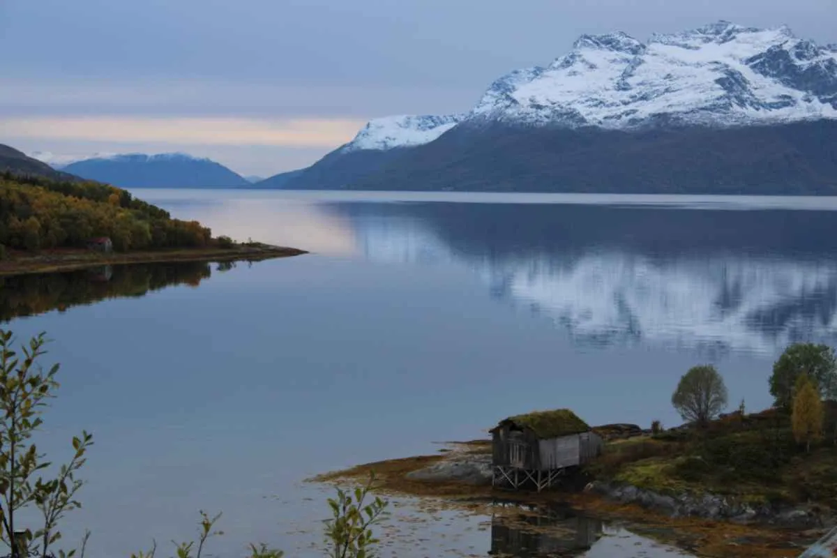 Elvelund, sul fiordo di Gratangen, con una capanna dal tetto di torba e le cime innevate che si riflettono nell’acqua calma.