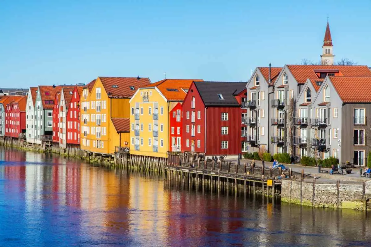 Oversiktsbilde av de typiske fargerike trehusene i den norske byen Trondheim, speilet i vannet rundt.