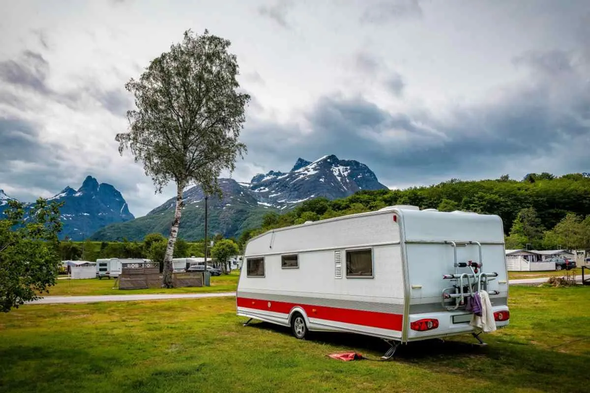 En bobil står parkert i et grønt norsk landskap med vegetasjon og andre kjøretøy rundt seg.