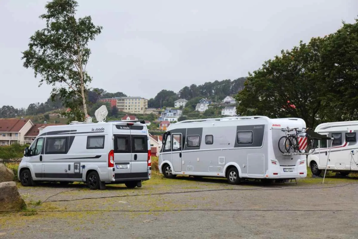 Camper parcheggiati in un campeggio a Narvik, in Norvegia, con case e colline boscose sullo sfondo in una giornata nuvolosa