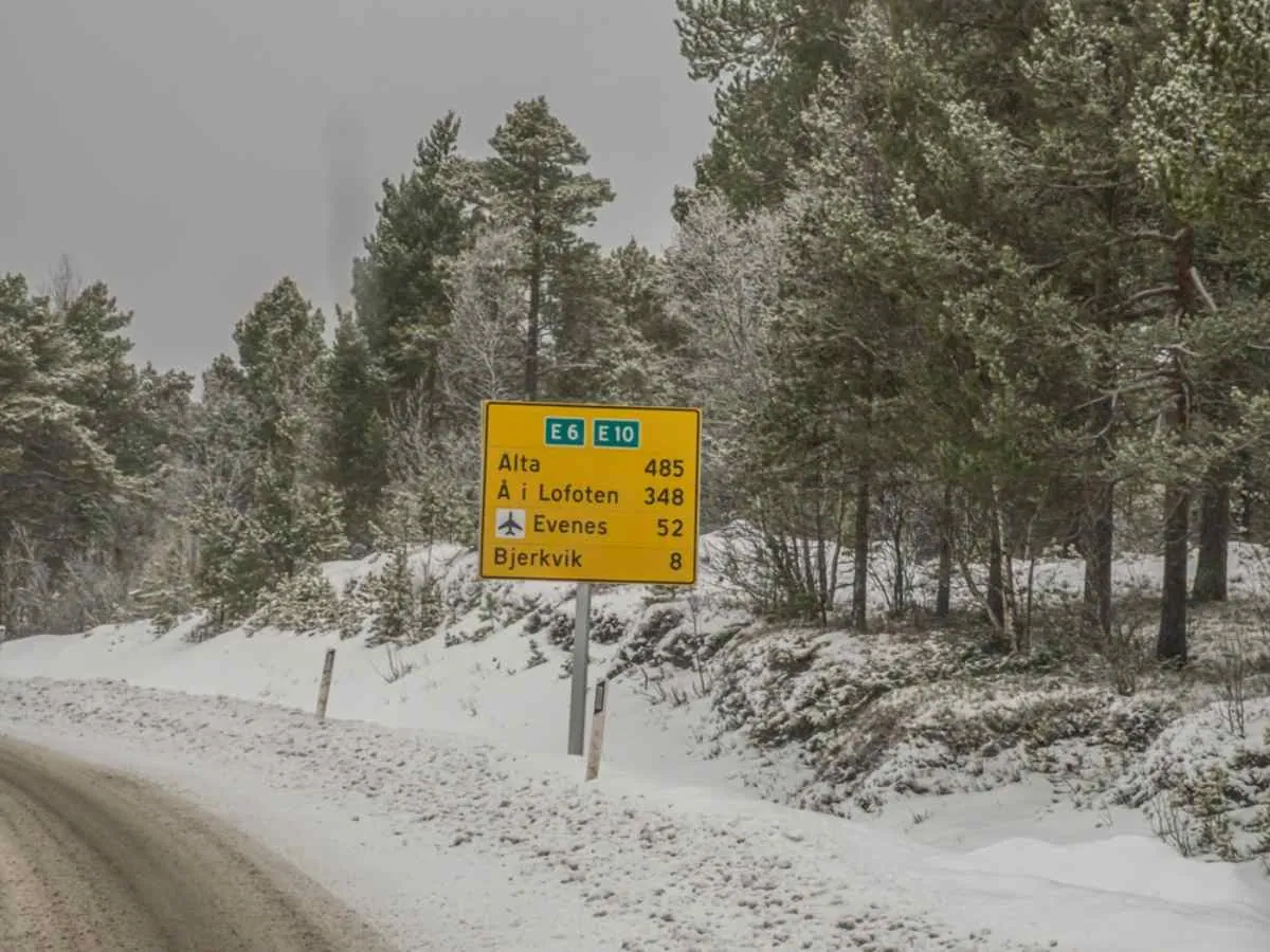 Vägskylt på den snötäckta E6-motorvägen i Norge som visar avstånden till Alta, Lofoten, Evenes och Bjerkvik.