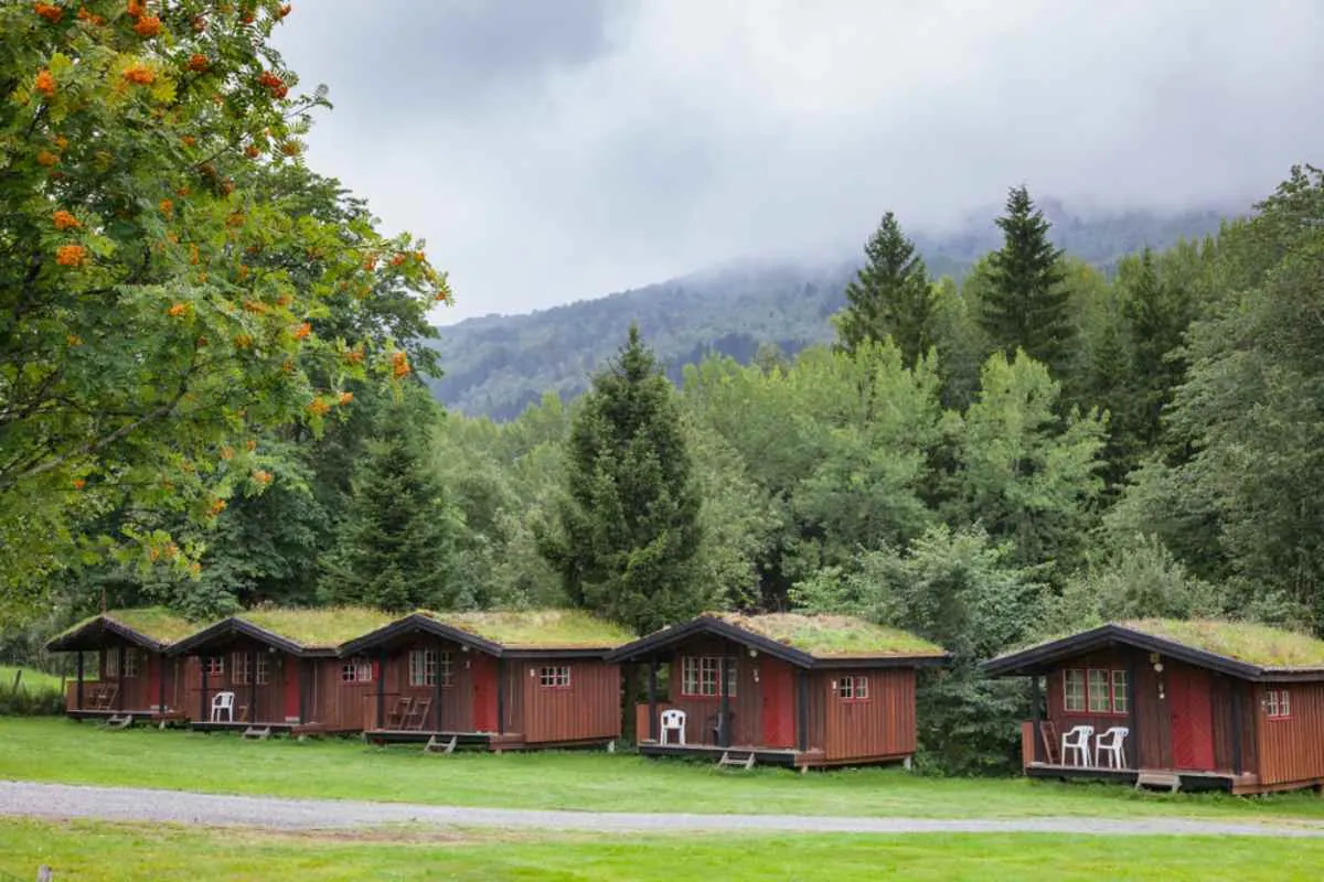 Une rangée de chalets en bois rouges et chaleureux aux toits verts dans un camping de la campagne norvégienne.