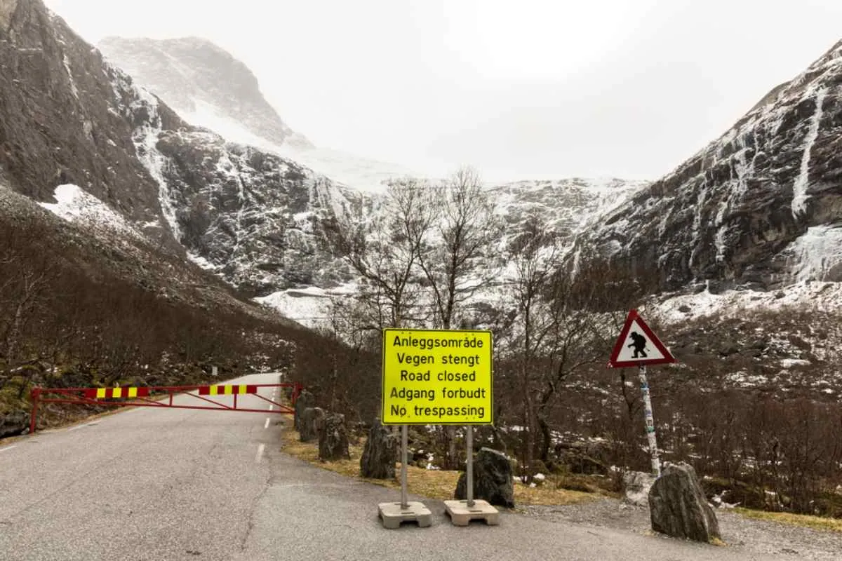 Gesamtansicht der norwegischen Trollstraße, die aufgrund von Unwettern gesperrt ist; ein gelbes Schild in der Landessprache weist auf diesen Umstand hin.