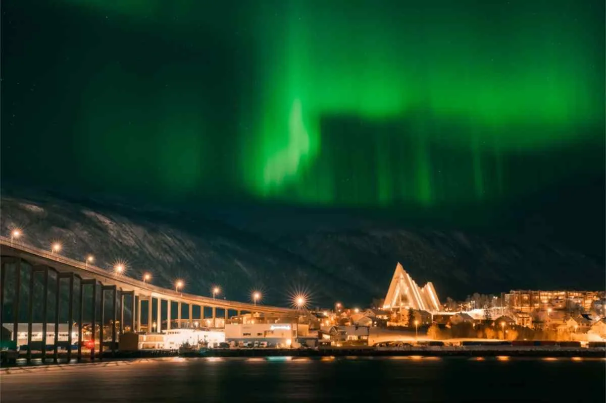 L'aurora boreale sopra un campeggio innevato vicino a Tromsø, con una tenda tipi illuminata, lanterne e corna di renna in primo piano di notte.