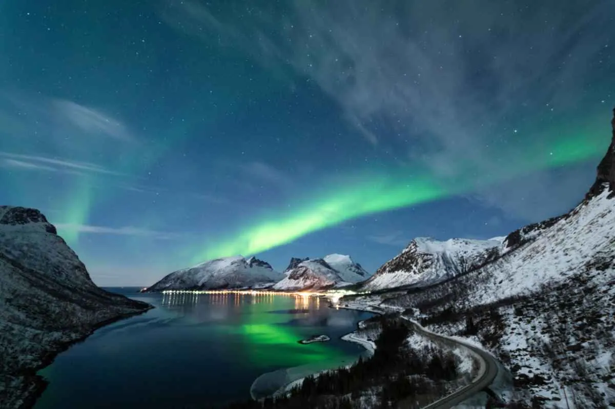 Appassionati di motoslitte che ammirano un’aurora verde brillante sopra le colline innevate vicino a Olderelv.
