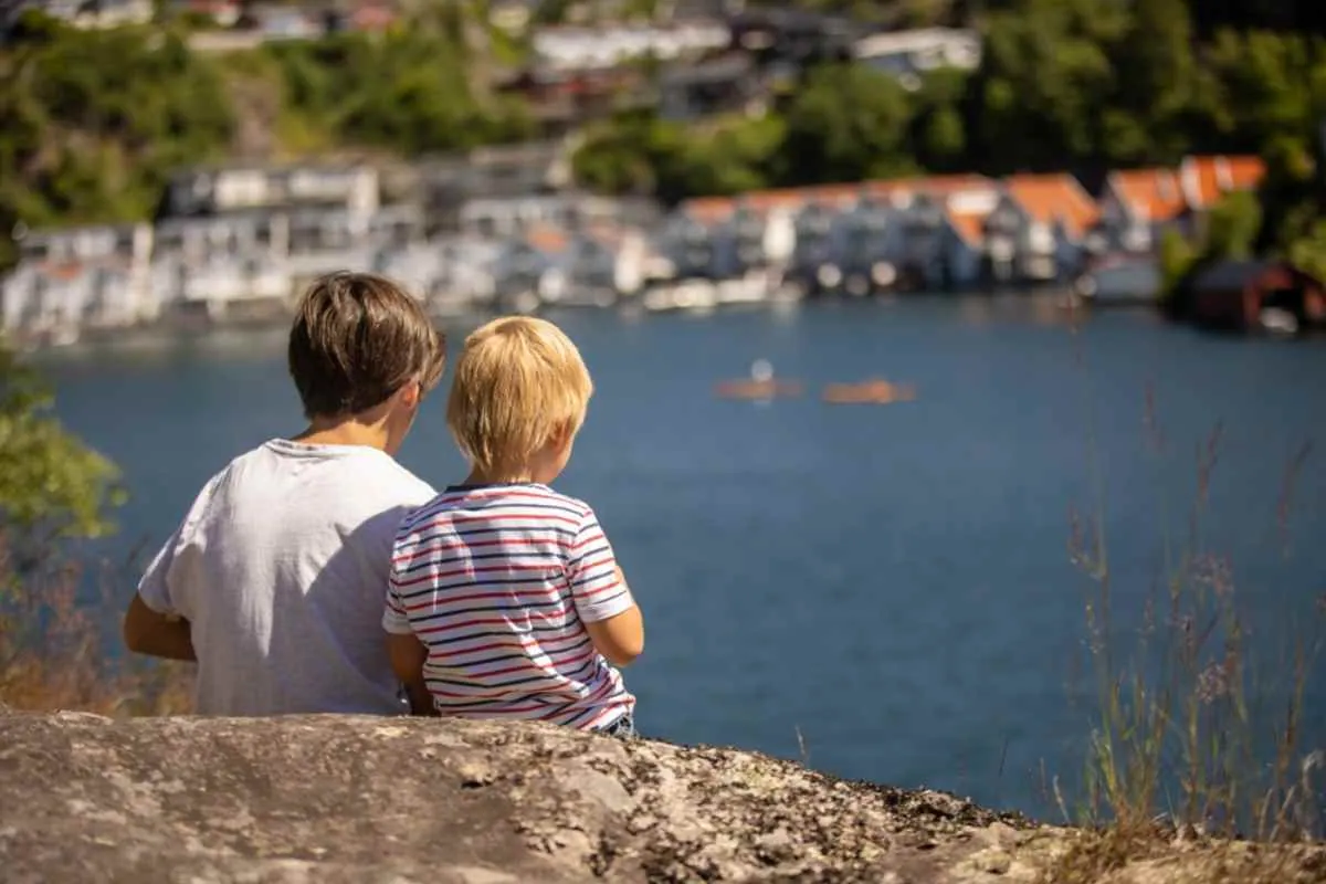 Två barn sitter på en sten med utsikt över hamnen i Flekkefjord vid E39.