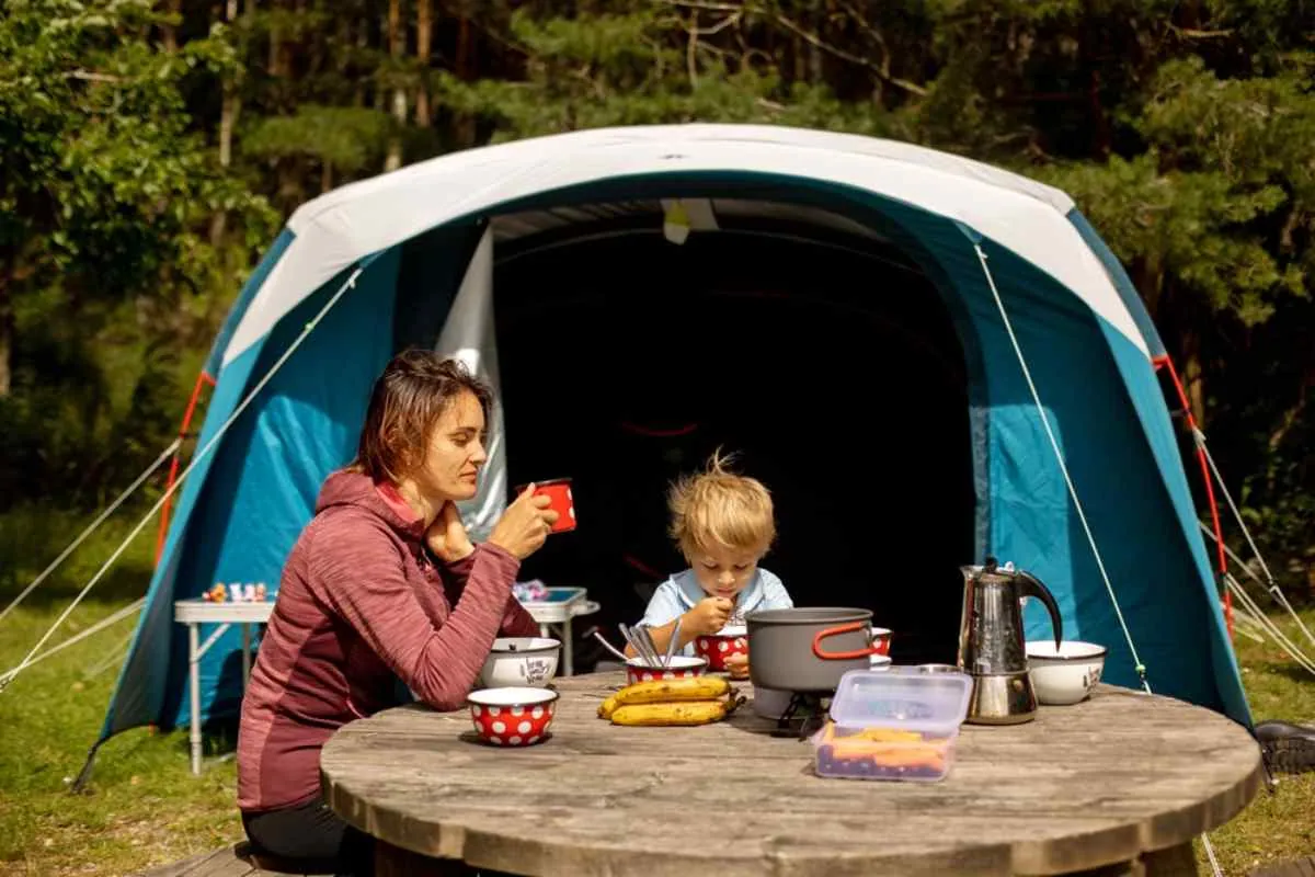 En familie som nyter et måltid utenfor et telt på en skogscampingplass i Norge, som illustrerer villcamping og friluftsliv.