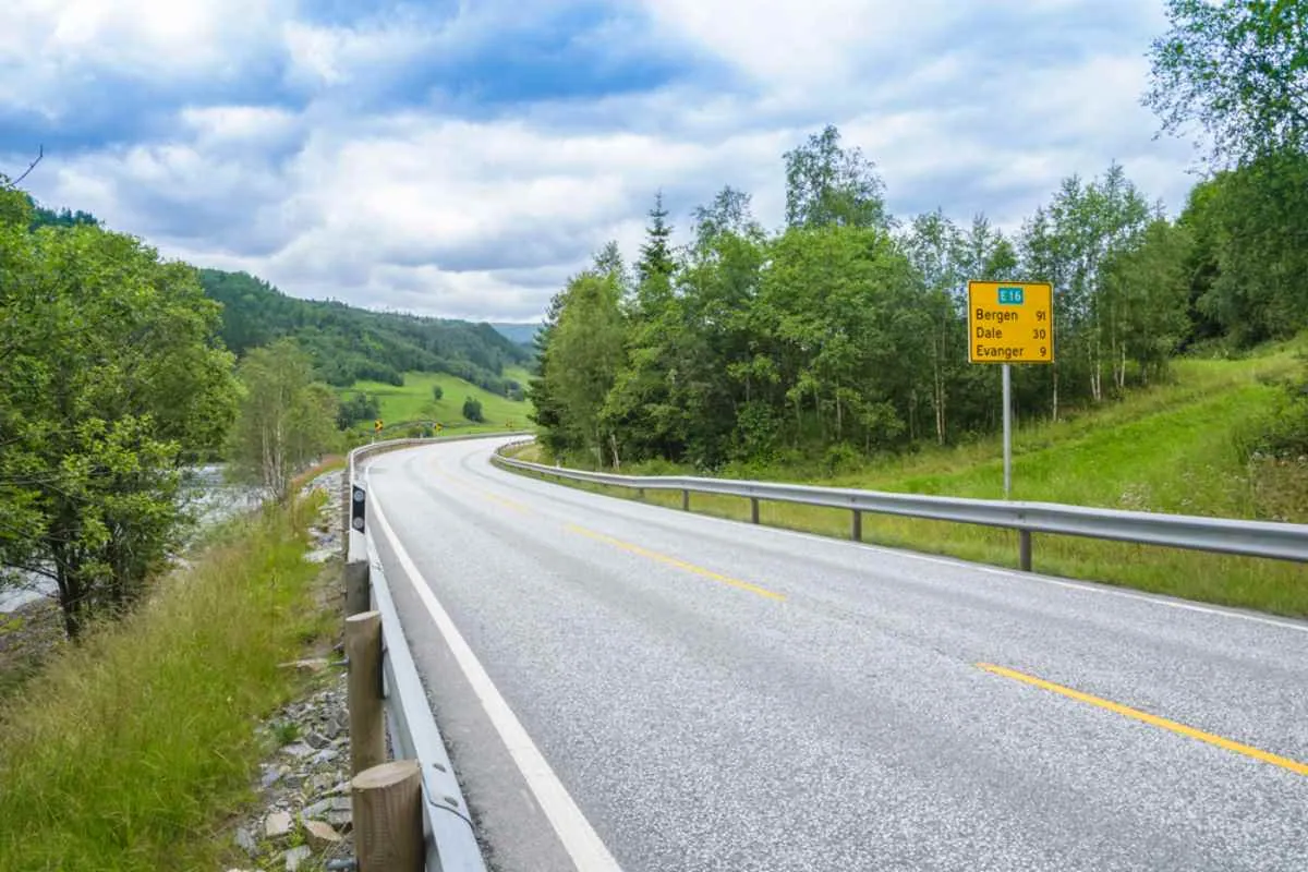 Die kurvenreiche E16 führt durch die grüne norwegische Landschaft, begleitet von einem gelben Schild, das nach Bergen, Dale und Evanger weist.
