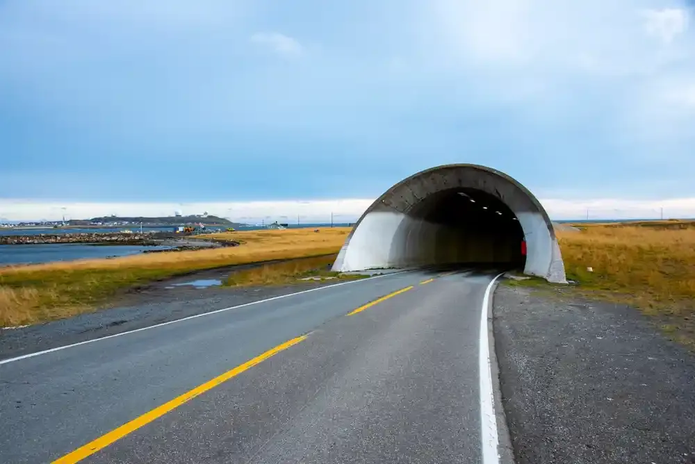 Veien fører inn i en betongtunnel gjennom gresskledde kystmarker under en skyet blå himmel.