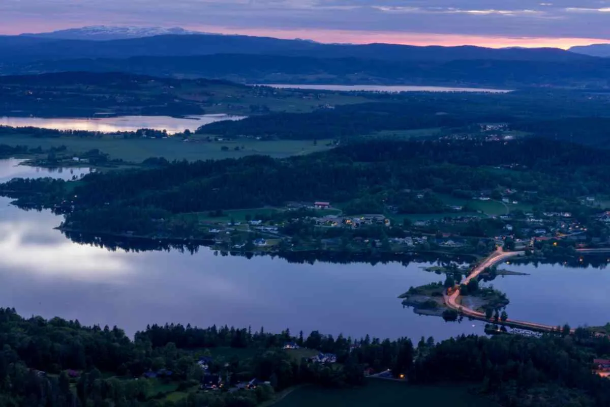 Oversiktsbilde av Tyrifjorden i Norge ved solnedgang. Man ser små landsbyer i en dal med rik vegetasjon og trær, omgitt av et stort vannområde.
