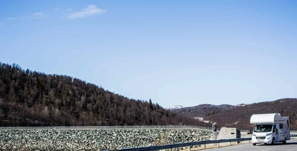 Hvit bobil på en naturskjønn norsk fjellvei under klar himmel, som viser at bobiler også betaler elektronisk bompenger på riksveiene.