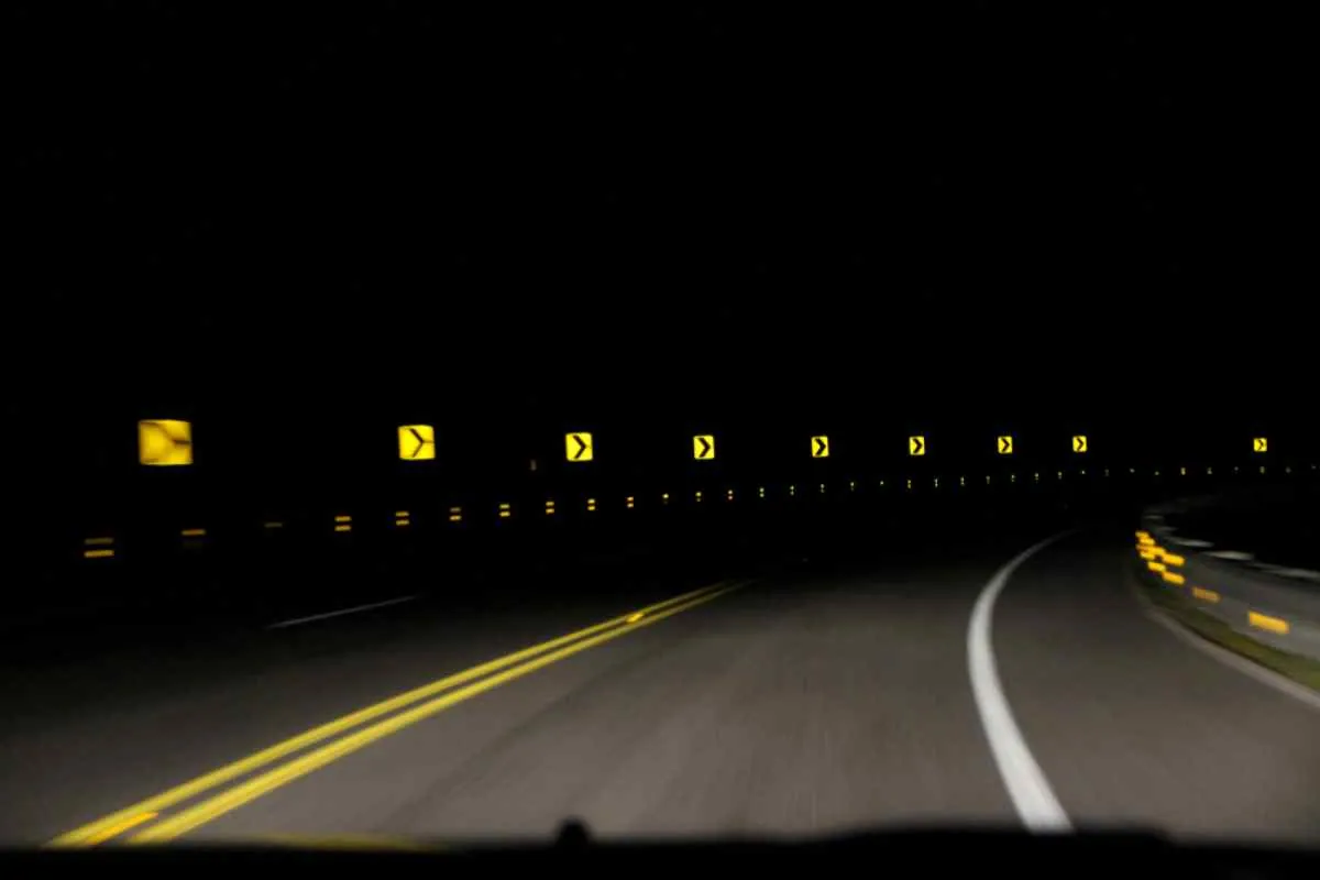 Gesamtansicht einer asphaltierten Straße mitten in der Nacht mit reflektierenden Verkehrszeichen, die von Fahrzeugscheinwerfern beleuchtet werden.