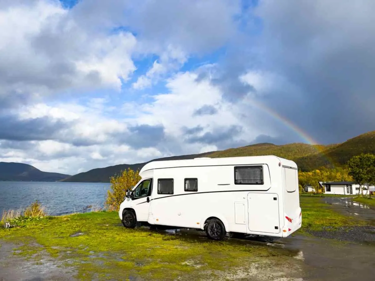 En hvit bobil står parkert på en norsk parkeringsplass i nærheten av det som ser ut som en fjord.
