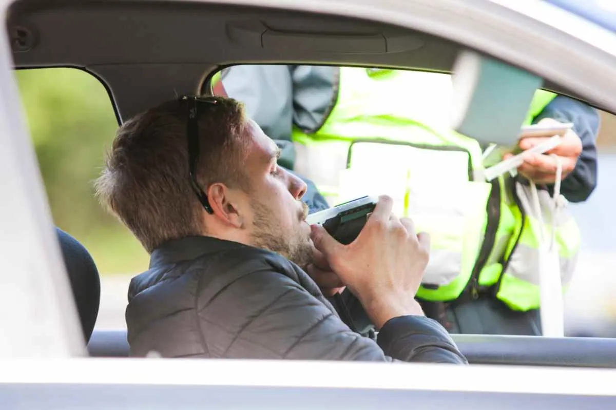 Un hombre rubio se somete a una prueba de alcoholemia sin bajarse del asiento del conductor de un coche aparcado frente a la policía de tráfico.