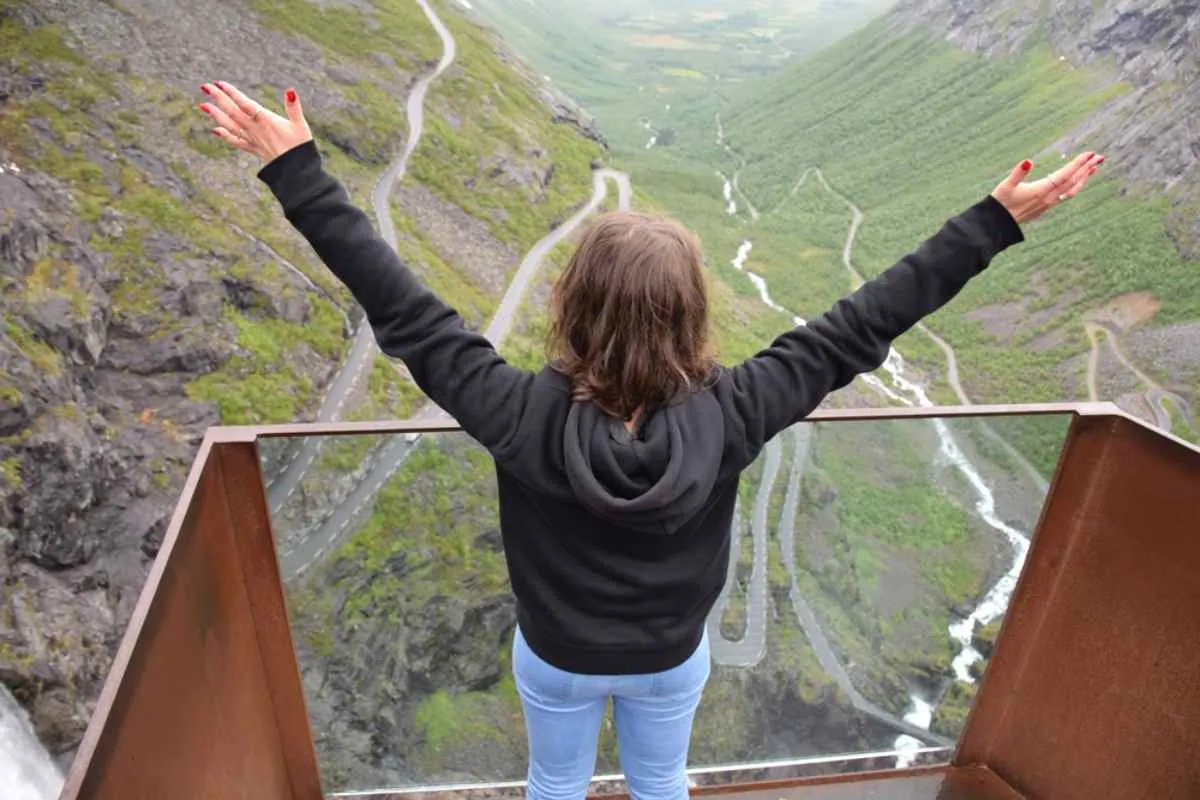 Eine Frau am Aussichtspunkt der norwegischen Trollstraße streckt ihre Arme vor dieser berühmten Straße in die Höhe.