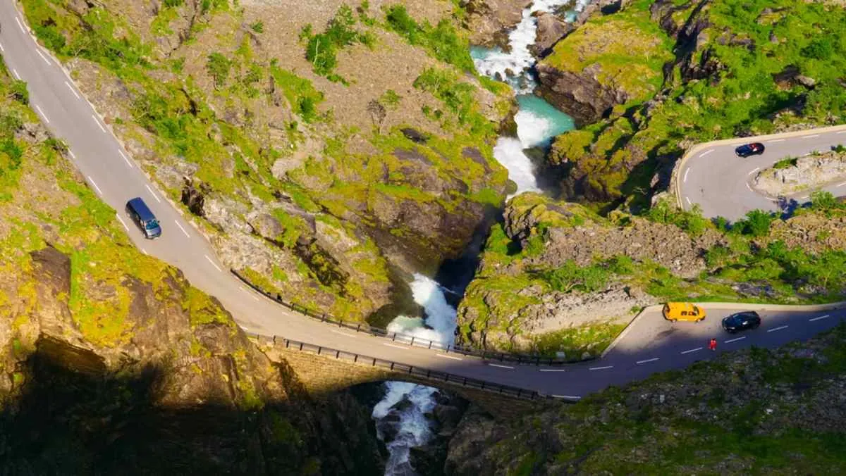 Drohnenaufnahme eines Abschnitts der norwegischen Trollstraße, die durch eine Art Fluss mit starker Strömung verläuft, auf dem mehrere Fahrzeuge fahren.