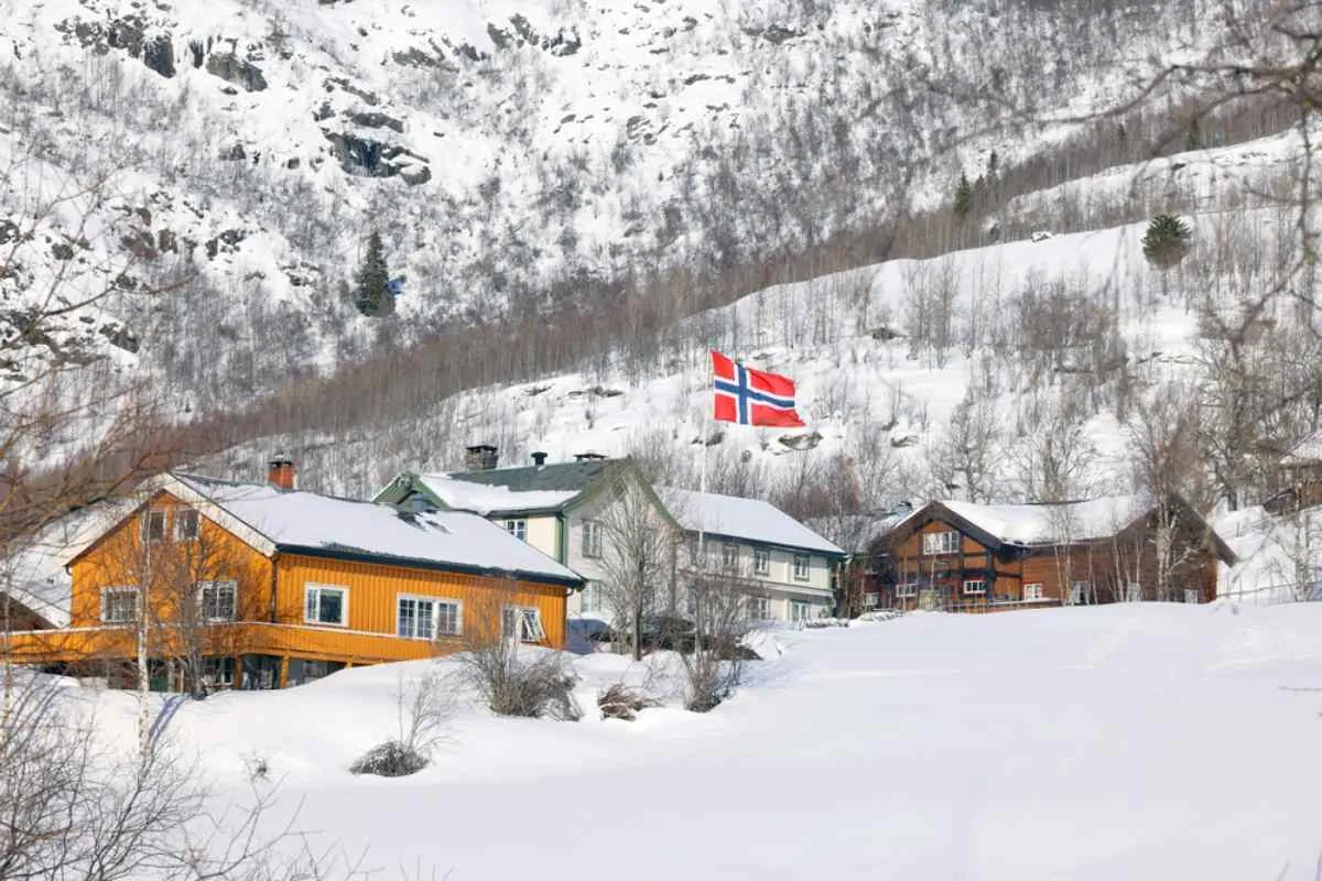 Tradisjonelle trehus i en snødekt norsk fjellandsby, med det norske flagget som vaier over hustakene.