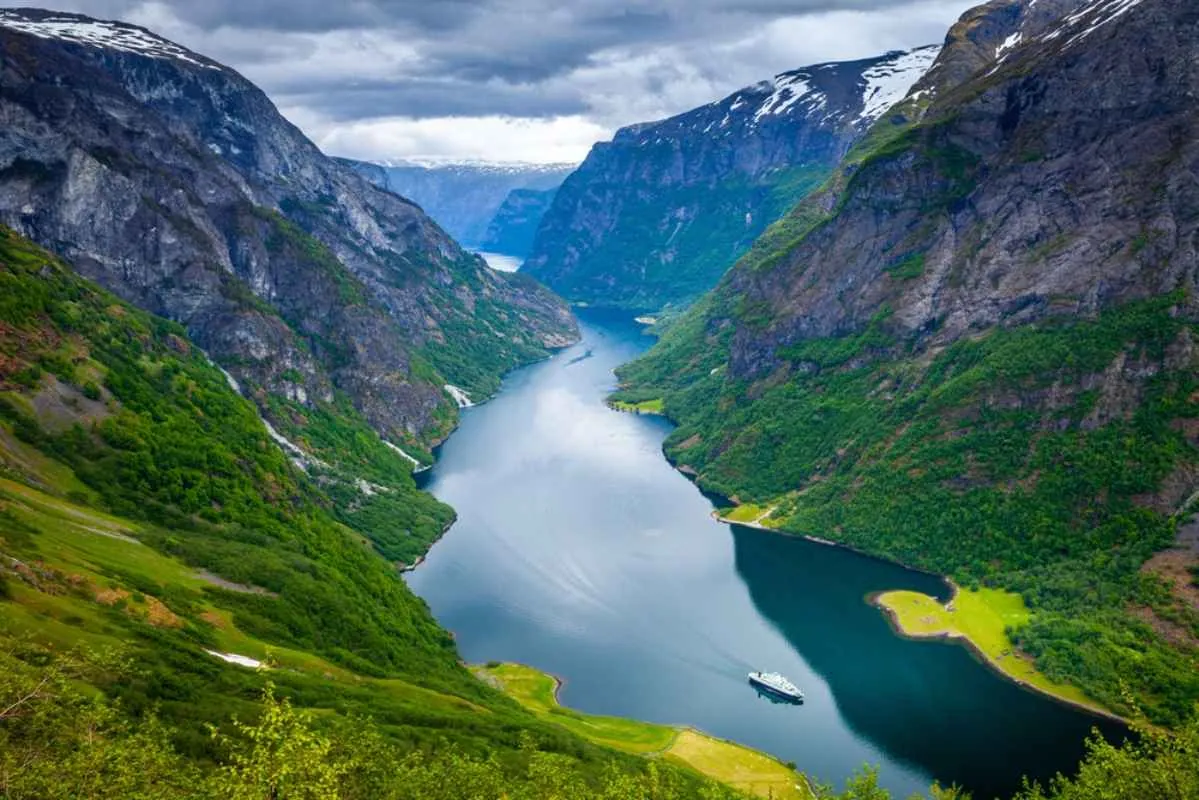Aussichtspunkt hoch über einem schmalen norwegischen Fjord mit steilen Bergen, grünen Hängen und einem Ausflugsboot auf dem Wasser.