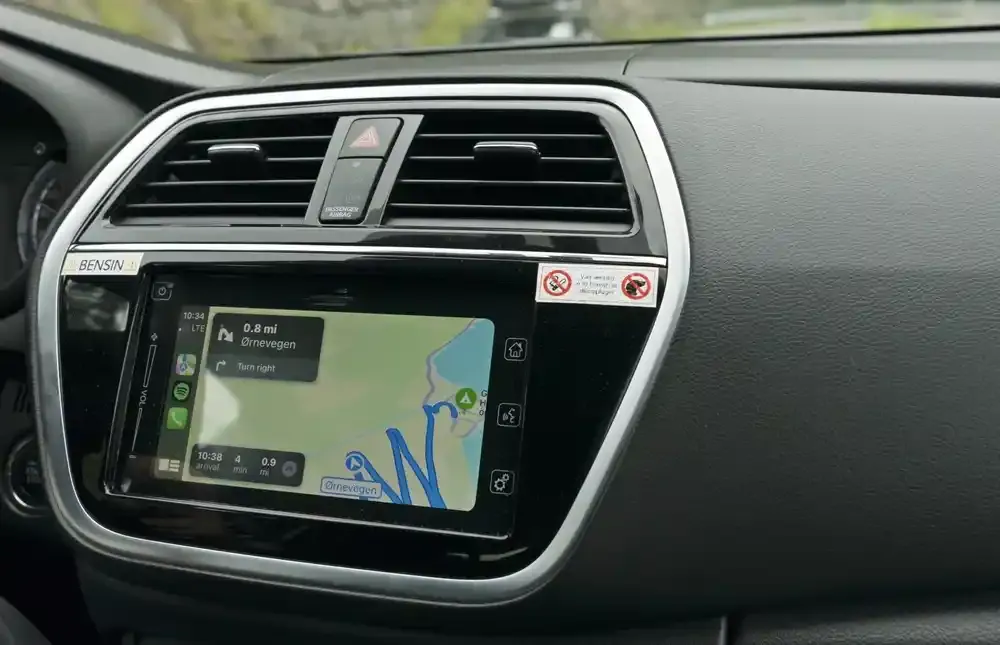 Berøringsskjermen på bilens dashbord viser et GPS-kart med «sving til høyre»-melding, blå rute, svart ramme og luftventiler.
