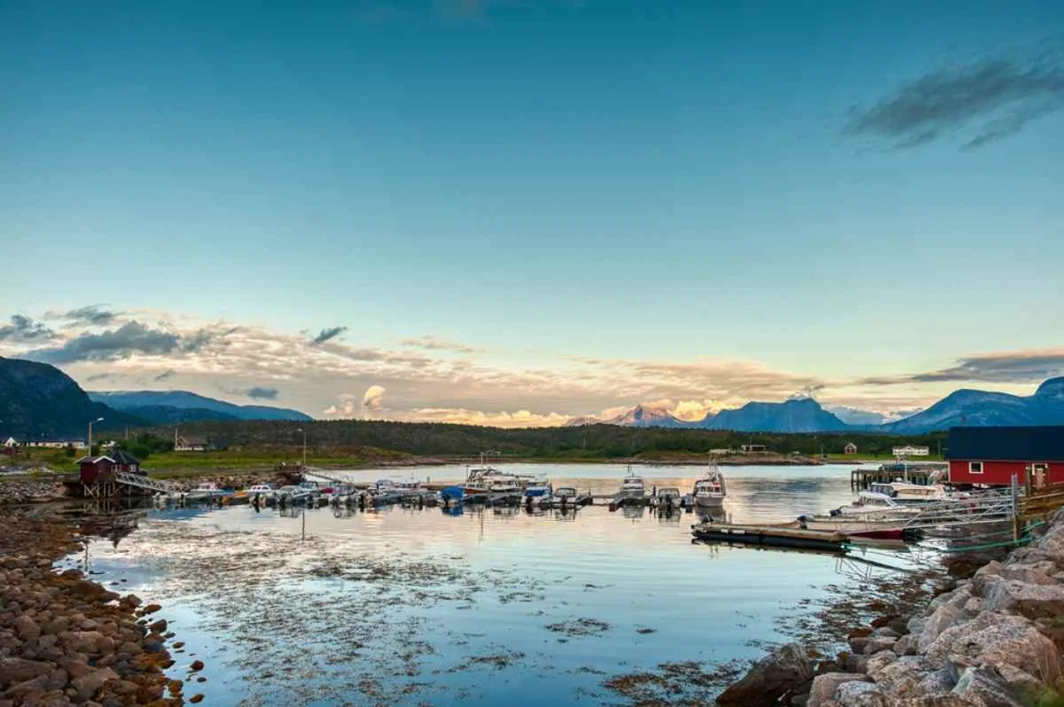 Tranquillo porto turistico vicino a Narvik con piccole imbarcazioni ormeggiate, le montagne in lontananza e l’acqua calma che riflette il cielo al tramonto