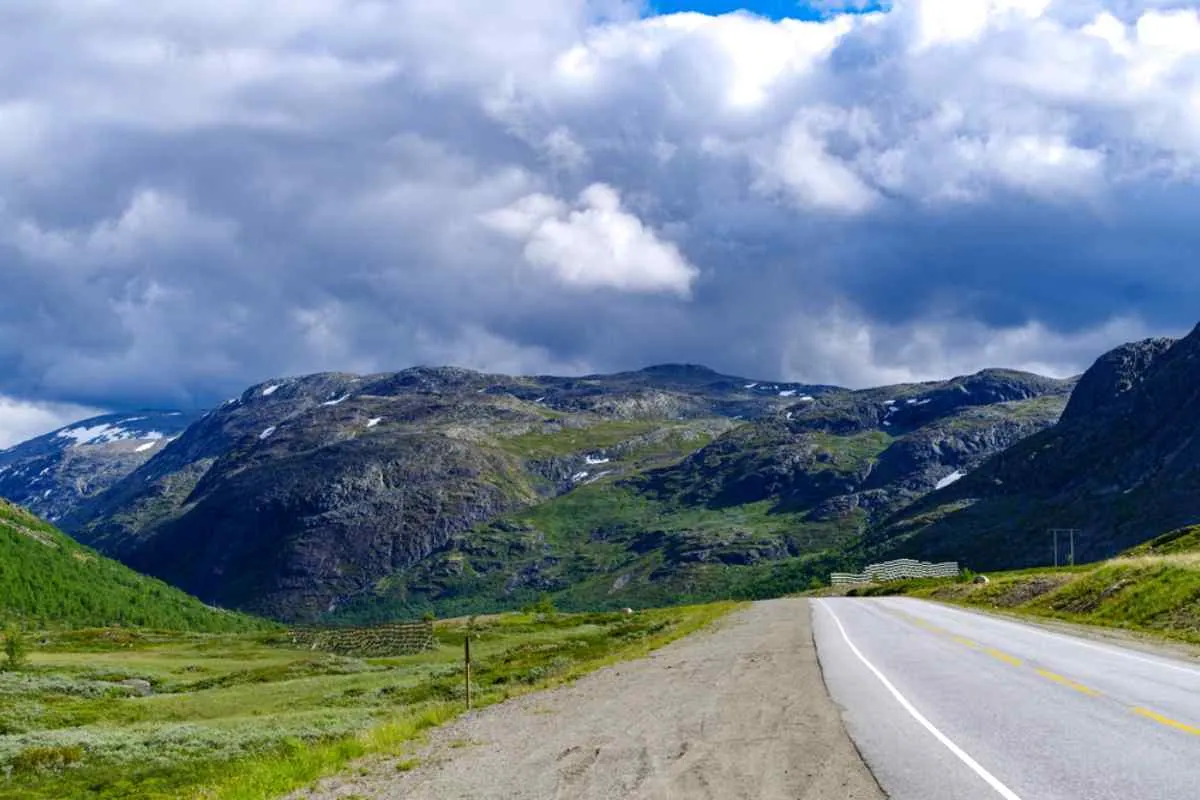 Naturskjønn strekning av RV Route 42 i Norge, som viser en åpen vei gjennom grønne fjell under dramatiske, skiftende værskyer.