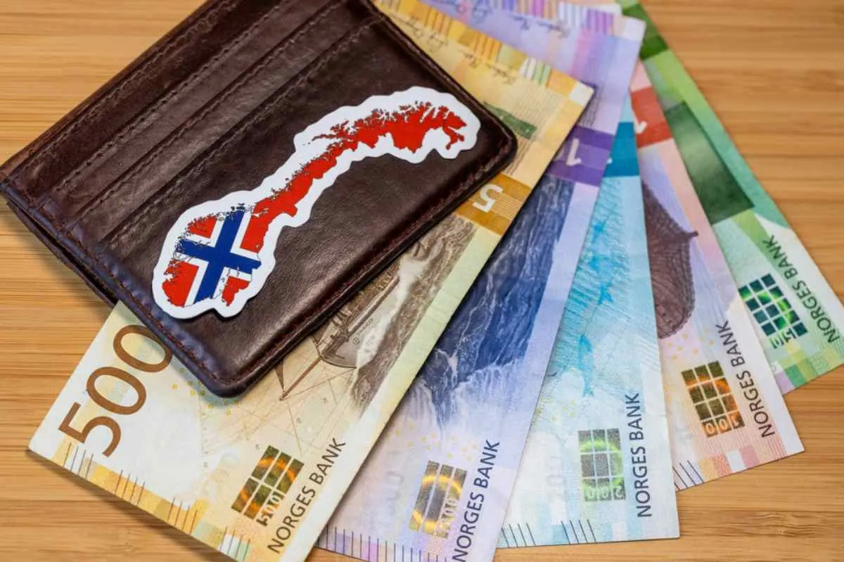 Norske sedler under en lommebok med et Norge-klistremerke, som illustrerer bompengekostnader og hvor mye sjåfører bør beregne i budsjettet for AutoPASS-avgifter.