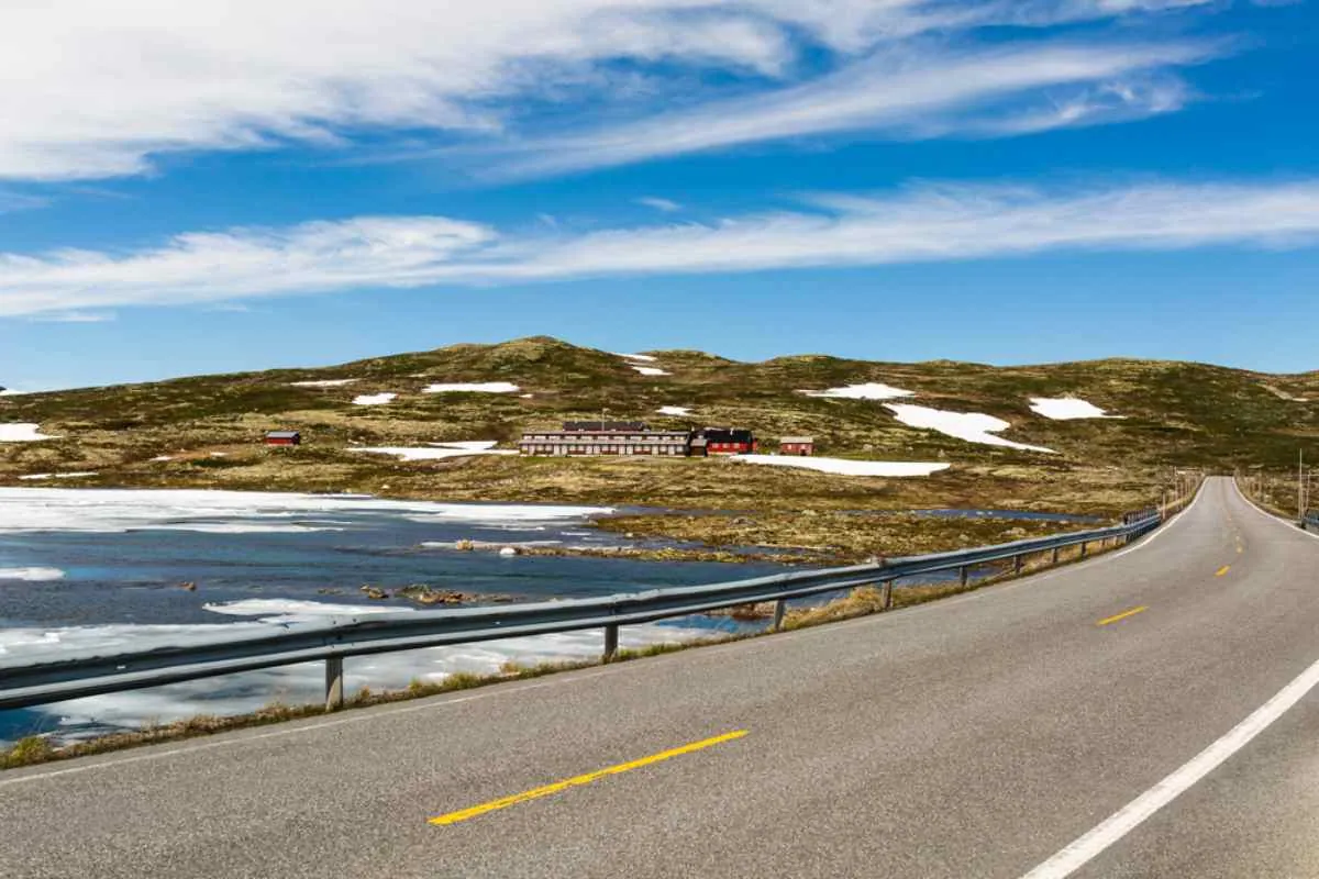 Rv7 passerer en delvis islagt innsjø og fjellhytter på en strålende vårdag i Norge.