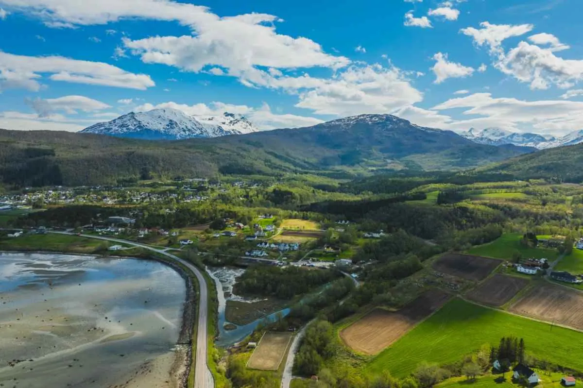 Vista aerea della valle di Narvik con strade costiere, campi verdi e montagne innevate sotto un cielo parzialmente nuvoloso