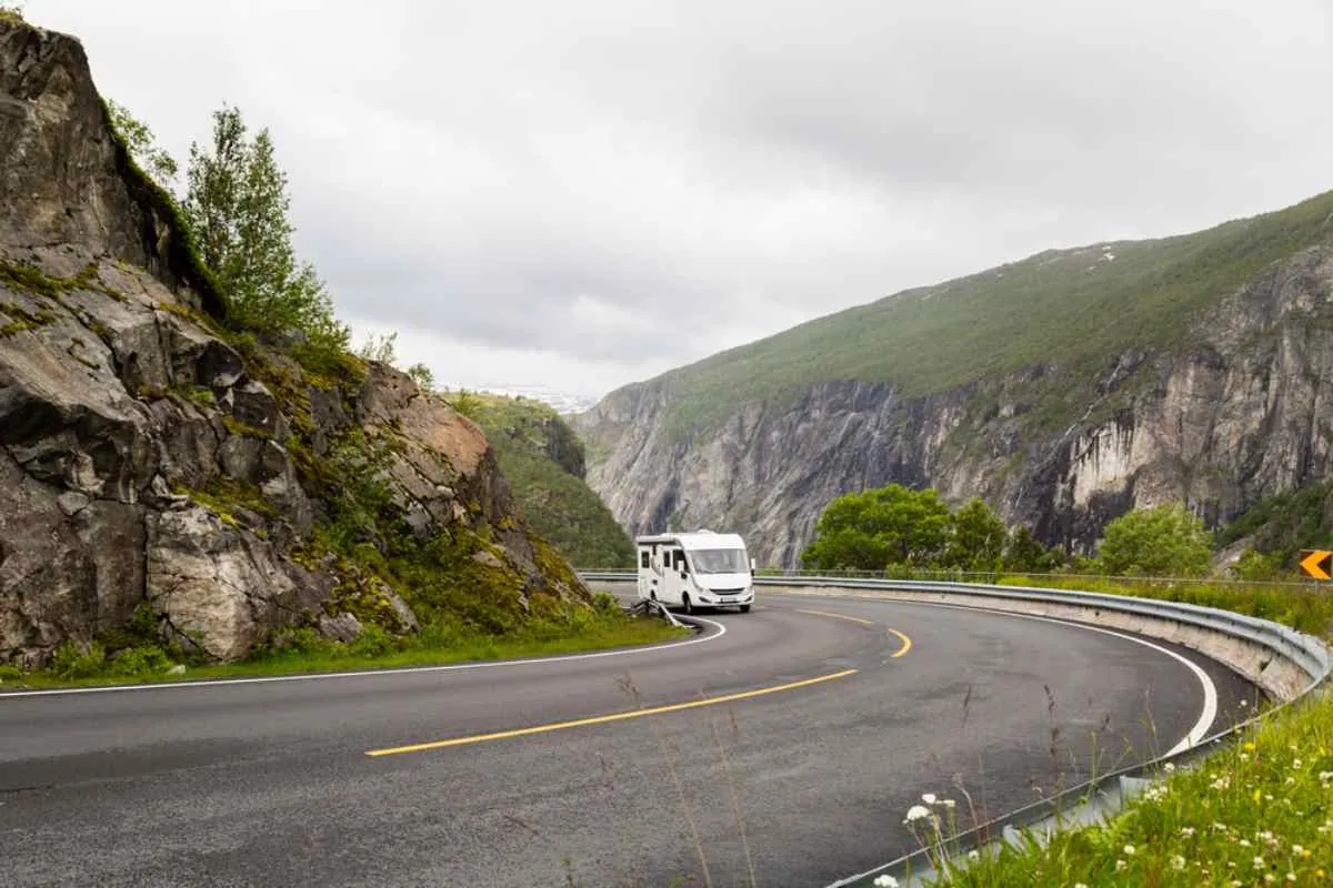 En bobil som kjører gjennom en skarp fjellkurve på den naturskjønne veien RV7 i Norge, nær bratte klipper.