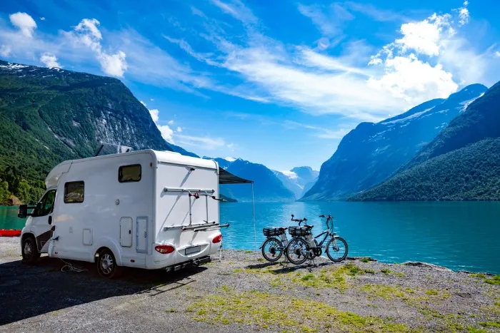 En familie på campingtur i Norge med en bobil ved innsjøen, med fjellene i bakgrunnen
