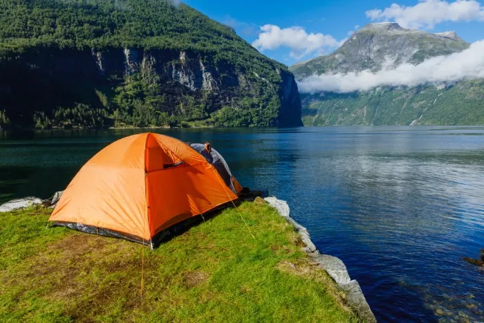 Turist på villcamping i Norge med spektakulær utsikt over en innsjø omgitt av fjell