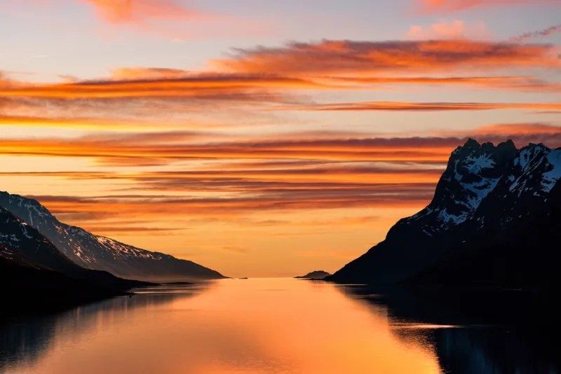 Wunderschöne Orangetöne in einem von Bergen umgebenen See – Mitternachtssonne in Norwegen