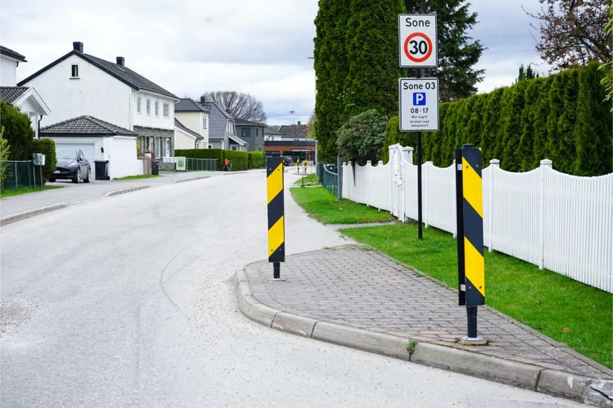Wohnstraße mit weißen Häusern und grünen Hecken. Das Tempolimit-Schild zeigt 30 an.